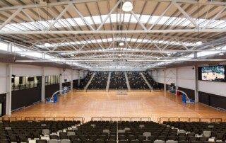 A photo of an indoor basketball court with banks of spectator seating