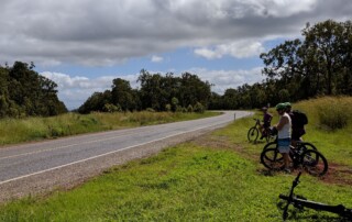 A photo of a group of three people on bikes on the side of a country road.