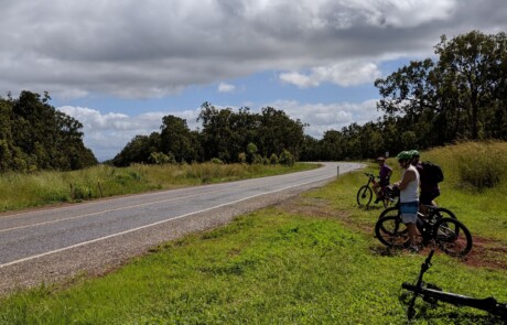 A photo of a group of three people on bikes on the side of a country road.